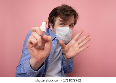 Coronavirus Protection And Disinfection Or OCD Concept. Caucasian Man In Medical Mask Spraying Sanitizer Spray Over Pink Background