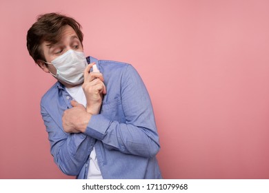 Coronavirus Protection And Disinfection Or OCD Concept. Caucasian Man In Medical Mask Spraying Sanitizer Spray Over Pink Background