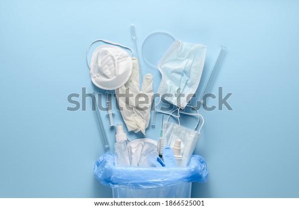 Coronavirus protection\
equipment in medical waste bin. Used disposable medical face masks,\
latex medical gloves, syringes and test tubes on pastel blue\
background. Flat\
lay