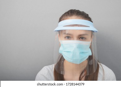 Coronavirus protection, health care and hygiene. Young woman in a protective mask screen with a visor on a gray background