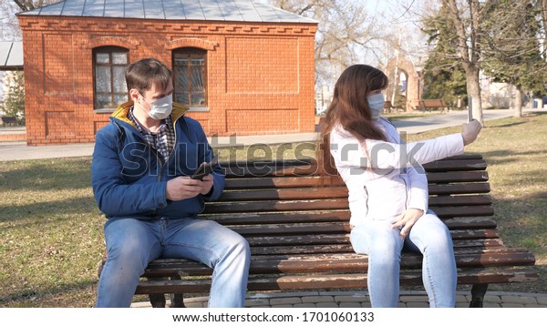 Coronavirus protection. woman and man in\
medical protective mask are sitting with smartphone on city street\
in Europe. Tourists on street wear a protective mask from viruses\
selfies on\
smartphone.