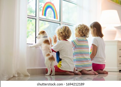  Coronavirus-Quarantäne. Bleib zu Hause. Kinder sitzen am Fenster. Kinder, die Regenbogen ziehen Zeichen der Hoffnung. Junge und Mädchen während des Corona-Virus sperren sich. Kind und Haustier. Die Isolation der Familie im Innenbereich. Prävention von Krankheiten
