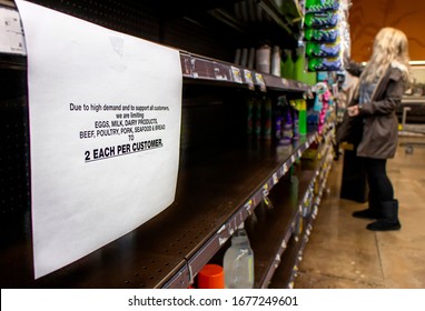 Coronavirus related sign rationing food at a supermarket with shopper in the distance - Shutterstock ID 1677249601