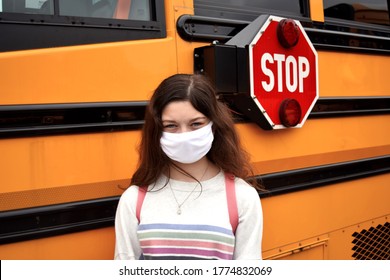 Coronavirus School Reopening Concept: A Girl Student Stands By A School Bus While Wearing A Face Mask And Backpack. Stop Sign Is Visible. Covid-19, Health, Safety, Education, Back To School Concepts.