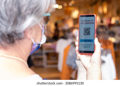 Coronavirus. Senior woman wearing face mask enters in shopping mall holding green pass application, vaccination passport for Covid-19 - Powered by Shutterstock