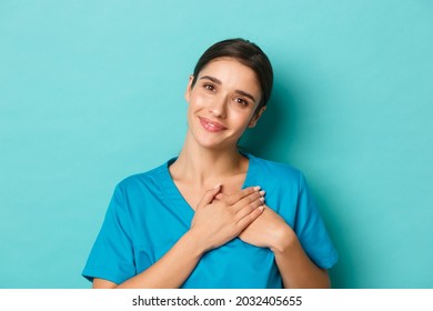 Coronavirus, social distancing and health concept. Close-up of smiling attractive female doctor, feeling grateful, holding hands on heart and looking with gratitude, standing over blue background