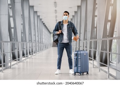 Coronavirus Travels. Young Middle Eastern Man In Protective Medical Mask Standing With Suitcase In Airport Terminal, Arab Male Tourist Waiting For Flight, Travelling During Pandemic, Copy Space