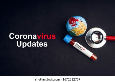 CORONAVIRUS UPDATES text with stethoscope, world globe and blood sample vacuum tube on black background. Covid-19 or Coronavirus Concept 
