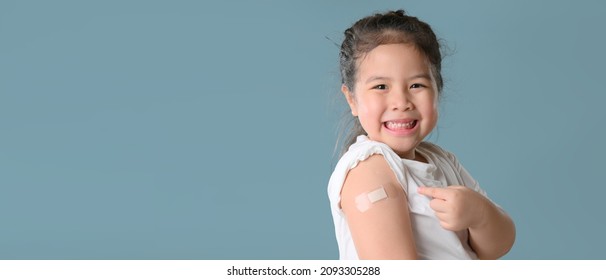 Werbung für die Impfung mit Coronavirus. Happy geimpftes kleines asiatisches Mädchen, das nach der Covid-19-Impfung auf blauem Hintergrund einen Arm mit Plaster-Bandage zeigt und dabei an die Kamera lächelt. Leerraum