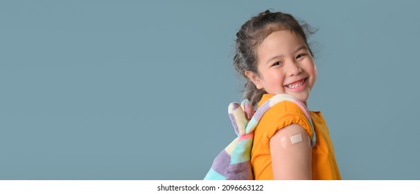 Werbung für die Impfung mit Coronavirus. Happy geimpftes kleines asiatisches Mädchen, das nach Covid-19-Impfstoff-Injektion einen Arm mit Plaster-Bandage zeigt und dabei an Kamera lächelt. Neue Normalität zurück zum Schulkonzept.