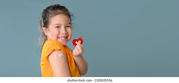 Werbung für die Impfung mit Coronavirus. Happy geimpftes kleines asiatisches Mädchen, das nach der Covid-19-Impfung auf blauem Hintergrund einen Arm mit Plaster-Bandage zeigt und dabei an die Kamera lächelt. Neu