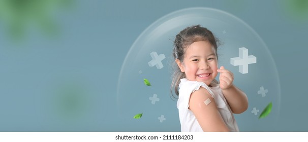 Coronavirus Vaccination Advertisement. Happy Vaccinated Little asian girl Showing Arm With Plaster Bandage After Covid-19 Vaccine Injection Posing Over Blue Background, Smiling To Camera.