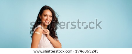 Coronavirus Vaccination Advertisement. Happy Vaccinated Woman Showing Arm With Plaster Bandage After Covid-19 Vaccine Injection Posing Over Blue Background, Smiling To Camera. Panorama, Blank Space