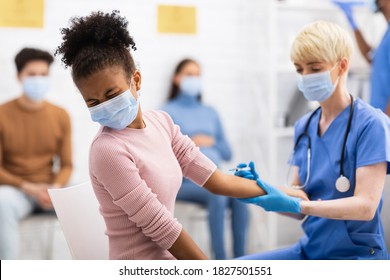 Coronavirus Vaccination. Black Teen Girl Receiving Covid-19 Vaccine Injection In Arm Sitting With Nurse In Hospital Room. Corona Virus Prevention, Cure And Medication Concept. Selective Focus