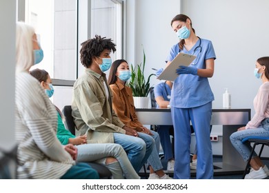 Coronavirus Vaccination Campaign Concept. Female doctor or nurse in uniform holding clipboard while talking to patients sitting and waiting in line at medical clinic, showing consent form to sign