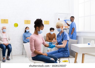 Coronavirus Vaccination Campaign. Nurse Giving Covid-19 Vaccine Injection To Black Teen Girl, While Multiracial Patients Sitting In Hospital Waiting Room. Corona Virus Population Immunization Concept