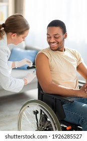 Coronavirus Vaccination For Disabled People At Home. Female Nurse Administering Covid-19 Vaccine Shot To Black Male Handicapped Patient In Wheelchair. Population Immunization Campaign