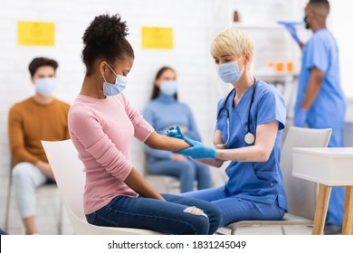 Coronavirus Vaccination. Nurse Vaccinating African Teenager Girl Against Covid-19 Injecting Corona Vaccine Injection Shot In Arm Sitting In Hospital. Covid 19 Virus Immunization Campaign