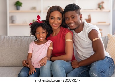 Coronavirus Vaccination. Vaccinated Black Family Of Three With Adhesive Bandage On Arms Posing At Home After Getting Covid-19 Vaccine Shot, Happy African Parents And Little Daughter Smiling At Camera