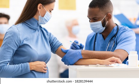 Coronavirus Vaccine. Black Doctor Making Vaccination To Pregnant Patient Woman Injecting Covid-19 Medicine Injection Sitting In Clinic. Corona Virus Medicine Cure And Treatment Concept. Panorama
