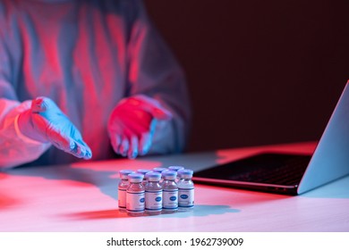 Coronavirus Vaccine. Virtual Research. Medical Online Collaboration. Female Scientist In Ppe Gloves Discussing Vial Dose On Laptop On Distance Videocall In Red Blue Neon Light In Dark Laboratory.