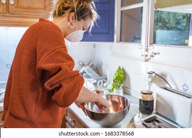 Coronavirus. Woman With Face Mask On Quarantine, Cooks In The Kitchen At Home During Coronavirus Crisis. Stay At Home. Enjoy Cooking At Home. Family Concept.