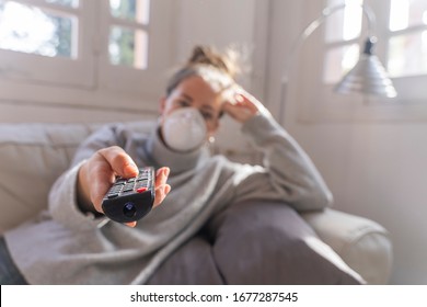 Coronavirus. Woman In Quarantine For Coronavirus Wearing Protective Mask, She's Watching Tv At Sofa. Stay At Home. Watch Tv On Quarantine. Protection. Health Care. 