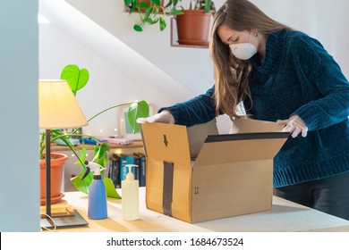 Coronavirus. Woman wearing a medical mask and rubber gloves receiving a package from a delivery man indoors. Virus prevention and protocols. Stay at home. Delivery service. Disinfecting the package. - Powered by Shutterstock