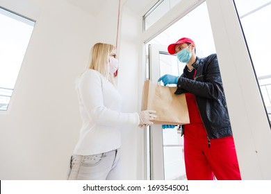 Coronavirus. Woman wearing a medical mask and rubber gloves receiving a package from a delivery man indoors. Virus prevention and protocols. Stay at home. Delivery service. Disinfecting the package. - Powered by Shutterstock