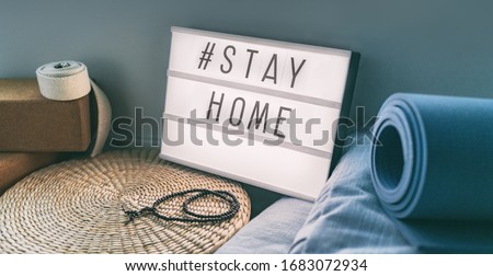 Coronavirus Yoga at home sign lightbox with text hashtag #STAYHOME glowing in light with exercise mat, cork blocks, strap meditation pillows. COVID-19 banner to promote self isolation staying at home.