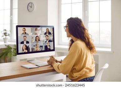 Corporate business team having a remote meeting. Young woman in casual clothes sitting at her desk at home, attending an online conference, looking at the computer screen, and smiling - Powered by Shutterstock