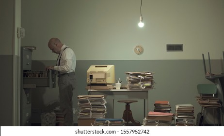 Corporate businessman searching for files in a rundown messy office with outdated computer and piles of paperwork