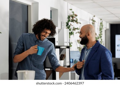 Corporate colleagues telling joke and laughing while drinking coffee in coworking space. Smiling young arab start up company employees enjoying work break in business office - Powered by Shutterstock