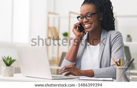 Corporate Communication. Black Businesswoman Talking On Mobile Phone Working On Laptop In Modern Office. Free Space