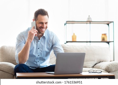 Corporate Communication Concept. Cheerful Businessman Making Phone Call, Typing On Laptop At Home. Free Space