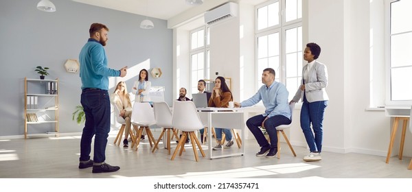 Corporate Company Manager Talking To His Multiethnic Business Team. Multiracial Group Of People Having A Work Meeting In A Beautiful Spacious Light Modern Office With Big Windows. Wide Angle Shot