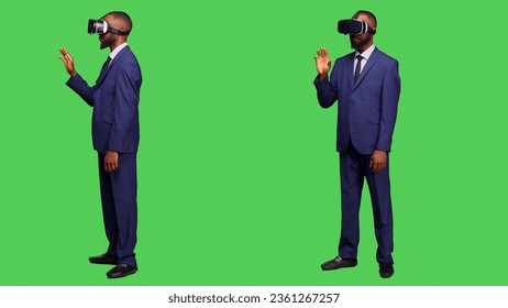 Corporate employee using vr headset on camera, working with virtual reality glasses and 3d simulation in studio. Young entrepreneur with modern device on full body green screen. - Powered by Shutterstock