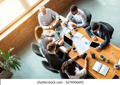 Corporate Lifestyle. Colleagues Working Together On Business Project Sitting At One Table In Modern Office. Above View