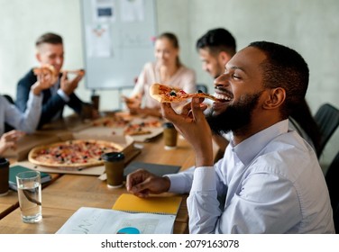 Corporate Lunch Break. Group Of Colleagues Eating Takeaway Pizza In Office, Happy Multiethnic Coworkers Enjoying Tasty Snack, Using Food Delivery Service At Workplace, Selective Focus On Black Man