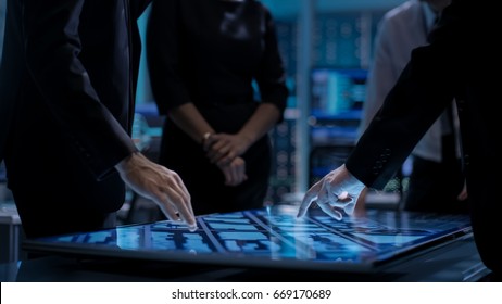 Corporate Managers Working At The Table In Monitoring Room. Room Is Full Of State Of The Art Technology. Computers With Animated Screens.