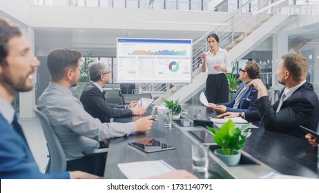 In The Corporate Meeting Room: Female Analyst Uses Digital Interactive Whiteboard For Presentation To A Board Of Executives, Lawyers, Investors. Screen Shows Company Growth Data With Graphs