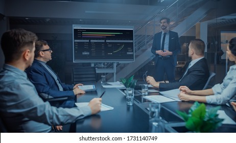 In The Corporate Meeting Room: Male Executive Talks And Uses Digital Interactive Whiteboard For Presentation To A Board Of Directors, Investors. Screen Shows Growth Data. Late At Night Office