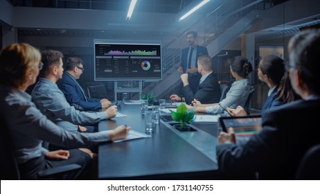 In The Corporate Meeting Room: Male Executive Talks And Uses Digital Interactive Whiteboard For Presentation To A Board Of Directors, Investors. Screen Shows Growth Data. Late At Night Office