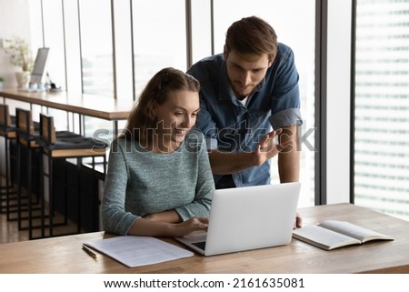 Corporate mentor teaching intern, giving advice, supervising work of new hired employee. Business coworkers, managers using laptop at workplace, watching and discussing content, Team work concept
