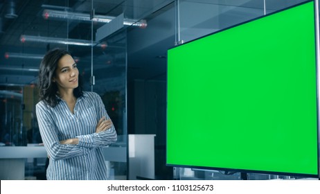 In The Corporate Office Beautiful Hispanic Woman Analyzes Green Screen Chroma Key Template Shown On A Wall TV.