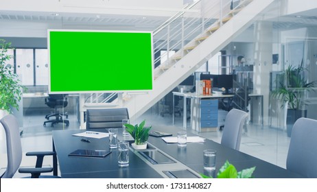 In The Corporate Office Meeting Room Stands Green Mock-up Screen TV Or Interactive Digital Whiteboard In Horizontal Mode. In The Background Big Bright Busy Office