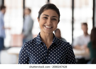 Corporate portrait of happy Indian female business team leader. Millennial employee looking at camera and smiling while group working in office behind her. Businesswoman, leadership concept. Head shot - Powered by Shutterstock