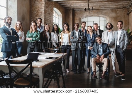 Corporate portrait of a multigenerational working team with multiracial and disabled members - Group photo of colleagues standing in the office in co-working space looking at the camera - lifestyle