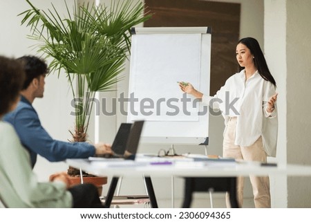 Corporate Presentation. Successful Japanese Businesswoman Presenting Her Project Ideas Pointing At Whiteboard Standing In Modern Office During Coworkers Meeting. Business Storytelling Skills