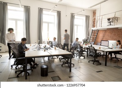 Corporate staff employees working together using computers at coworking, busy workers group walk in motion sitting at desks in modern open space room interior, everyday office rush lifestyle concept